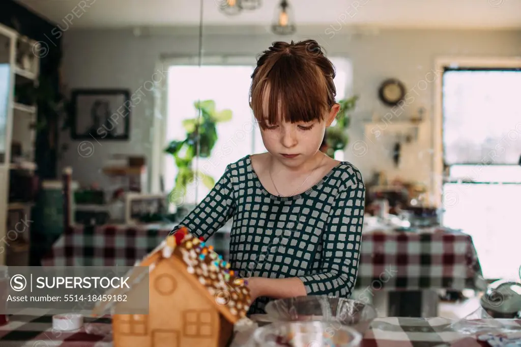 Young girl decorating a gingerbread house inside