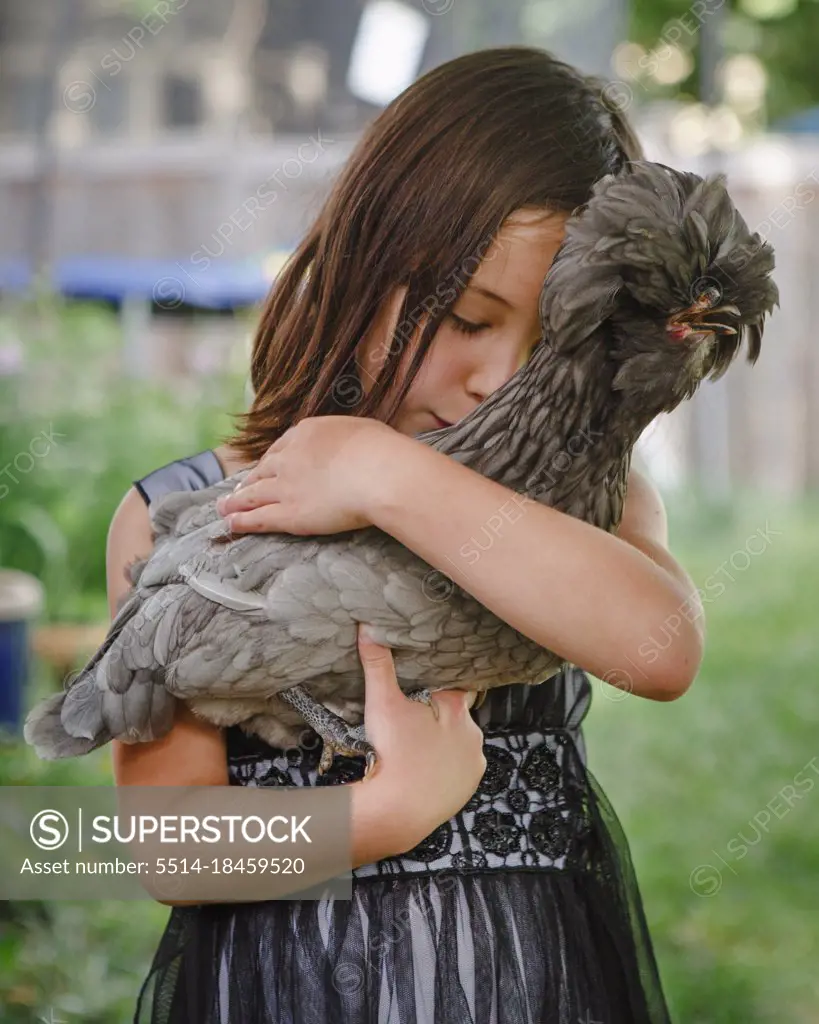 Beautiful girl, eyes closed, tenderly holds a pet chicken in her arms