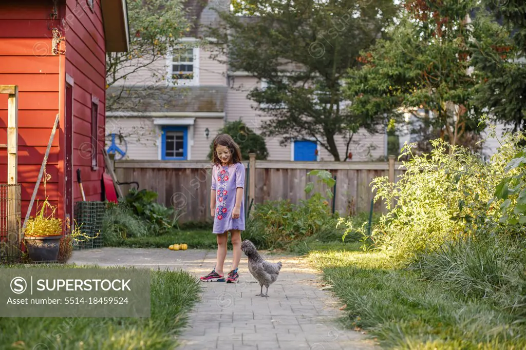A smiling girl plays with her pet chicken outside in sunlit garden