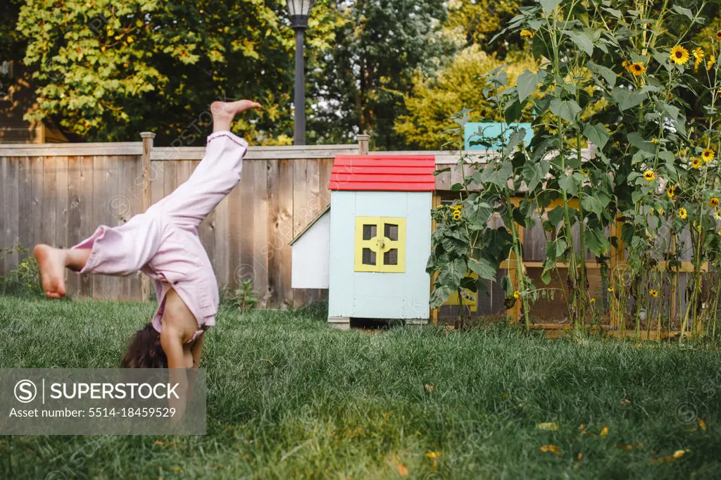 A little girl cartwheels in backyard by colorful chicken coop