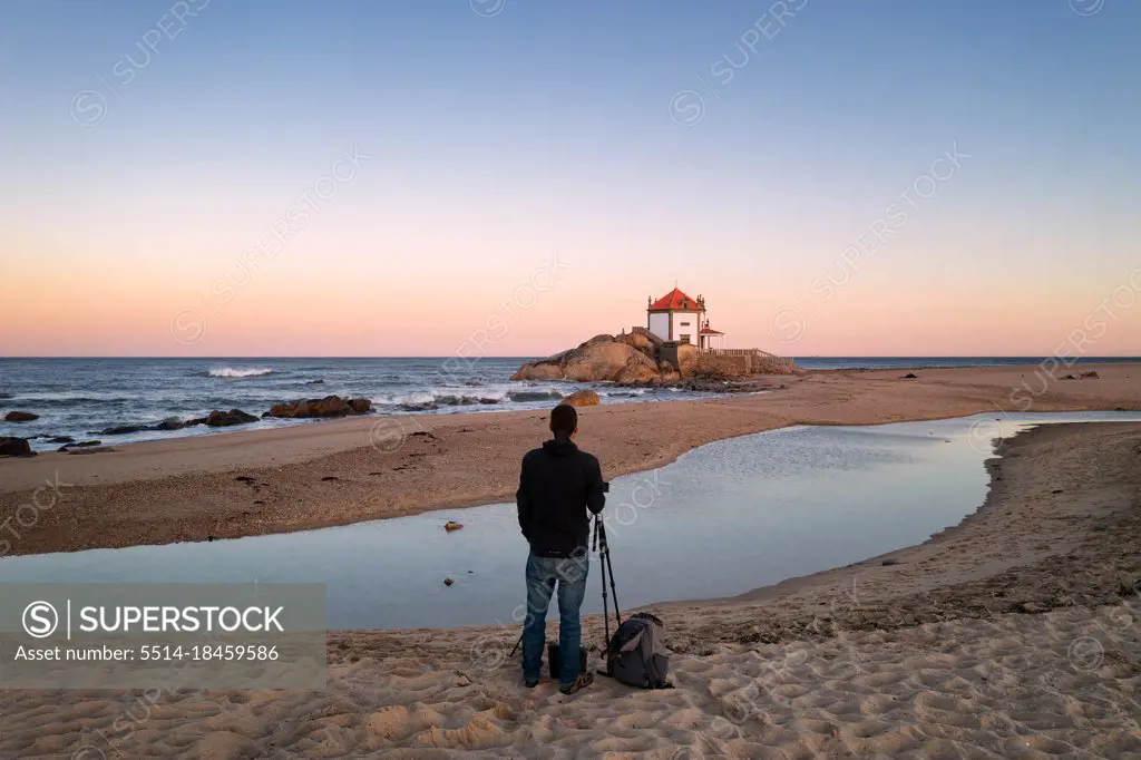 Man photographing beautiful Senhor da Pedra chapel on the beach