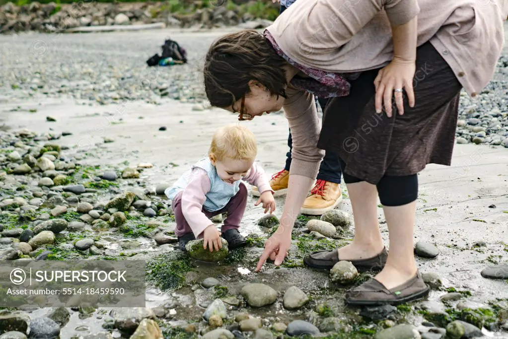 Closeup portrait of a mother and daughter looking under beach rocks