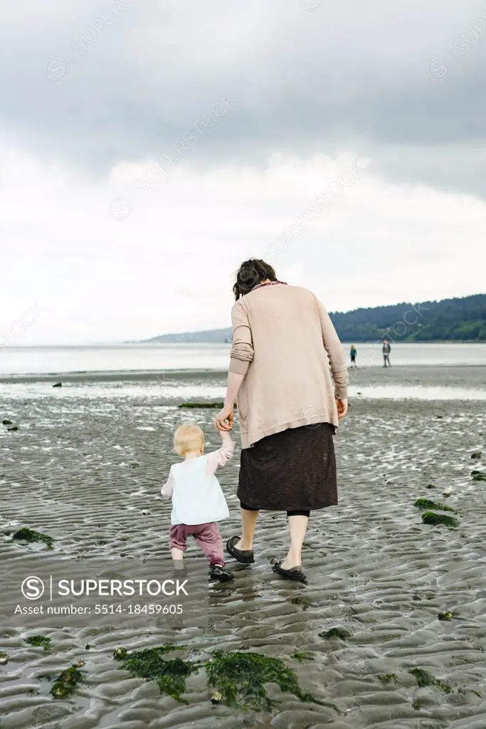 View from behind of a mother and daughter holding hands on the beach
