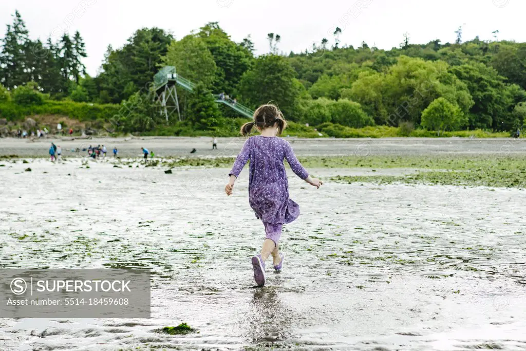 View from behind of a child running on a wet, sandy beach