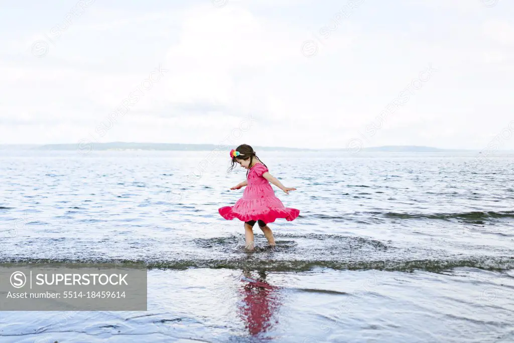 Wide angle view of a young girl twirling in the beach waves
