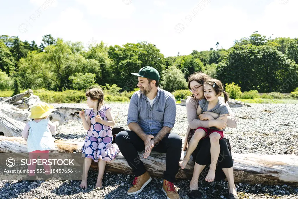 Straight on view of a family sitting on driftwood together at a beach