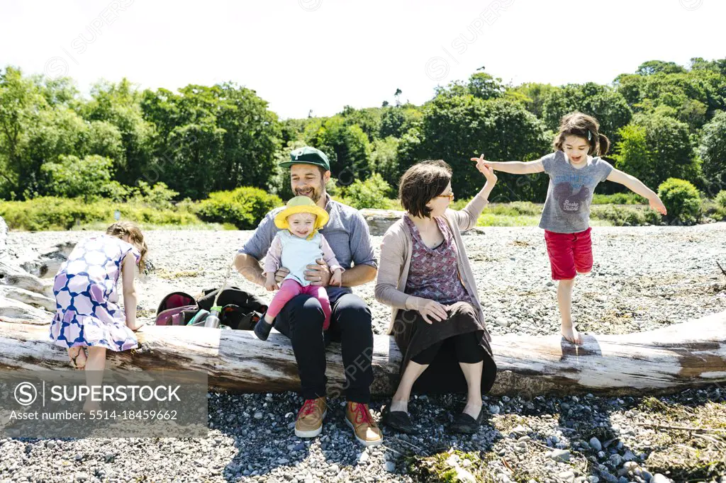 Wide view of a mother helping her daughter balance on driftwood