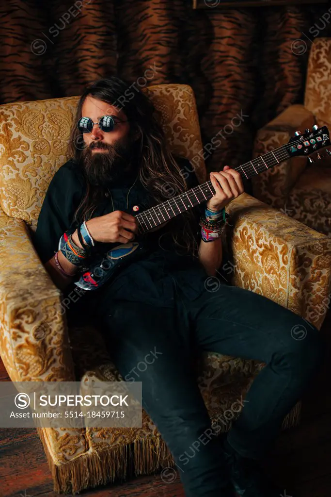 Man in black playing electric guitar while resting in arm chair