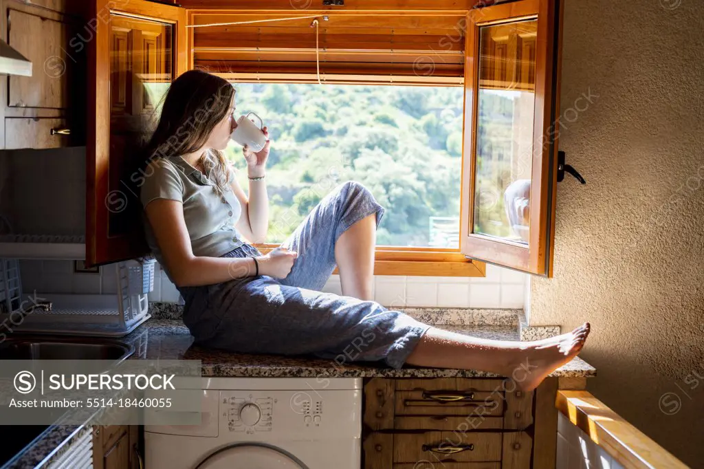 Teenage woman sitting looking out the window drinking coffee