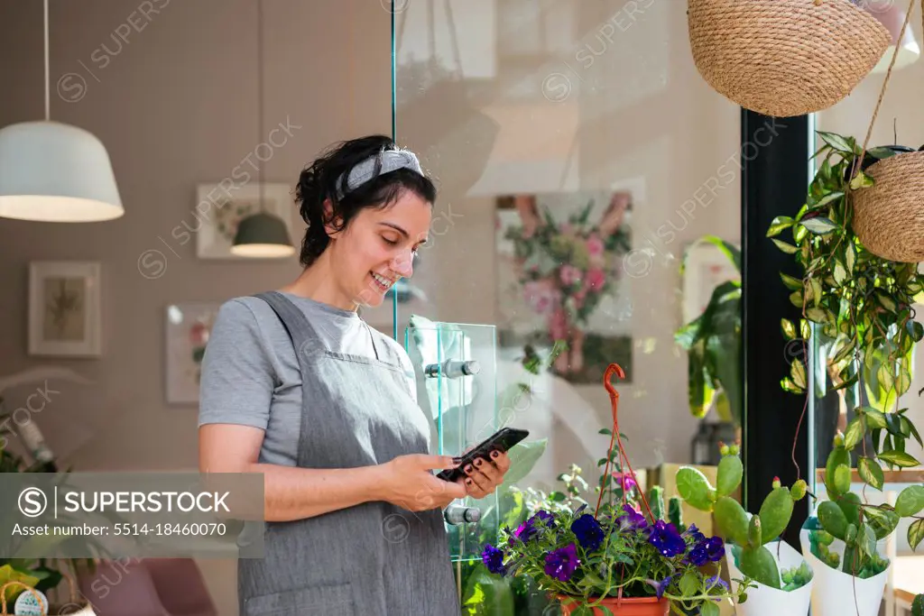 Florist standing at the door of her flower shop using a smartphone