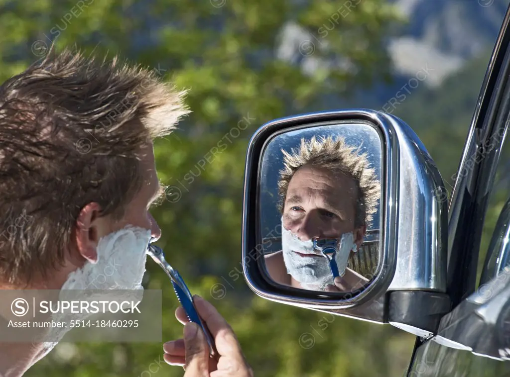 man shaving in the side mirror of his car on roadtrip