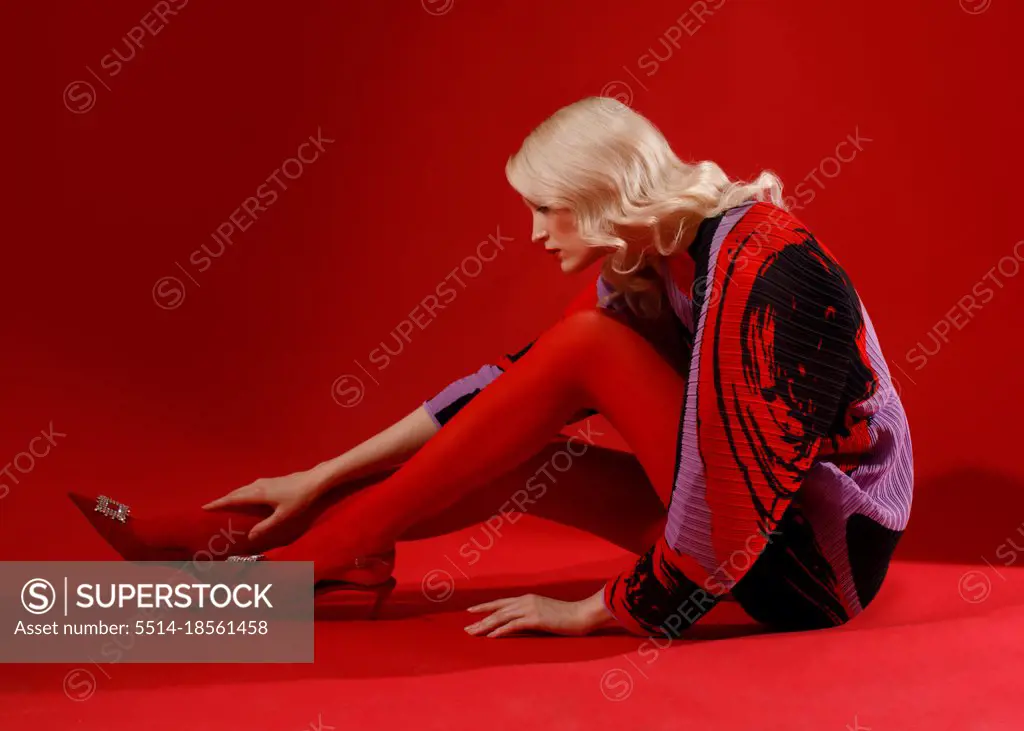 fashion woman in red dress and tights sitting on red studio background