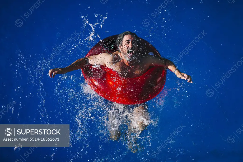 66-year-old man enjoying a sunny day in the pool with a red float