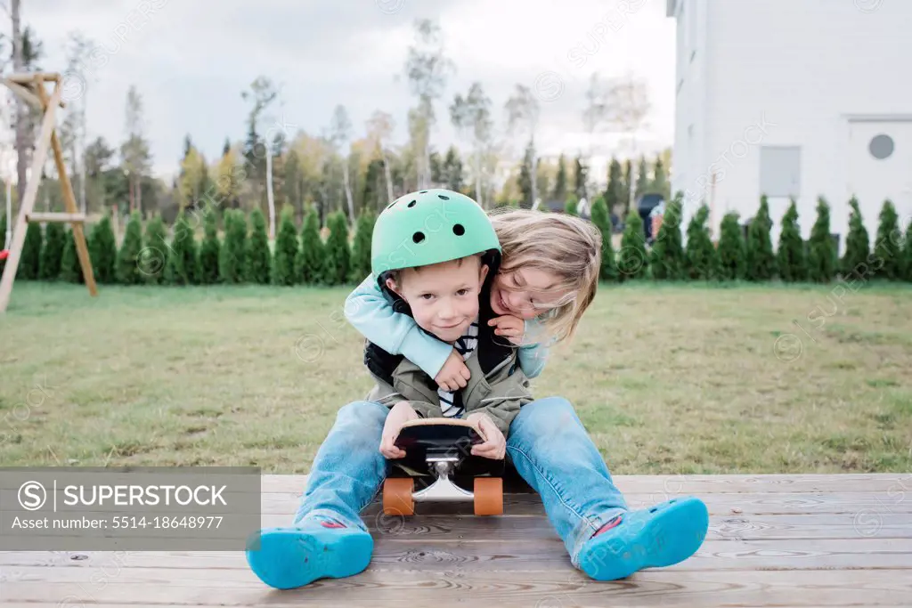 sister hugging her brother whilst playing on a skateboard outside