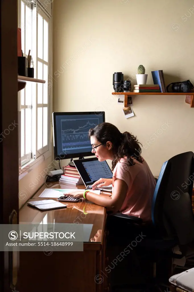 Female broker trading on stock market using laptop from home office.