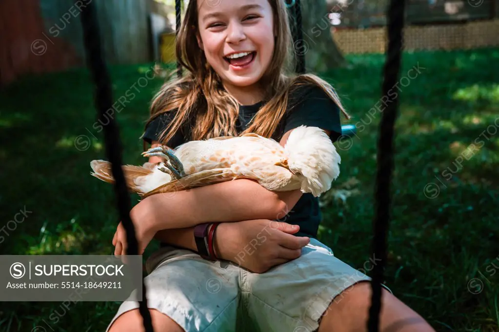 Young girl laughing while swinging with her pet chicken