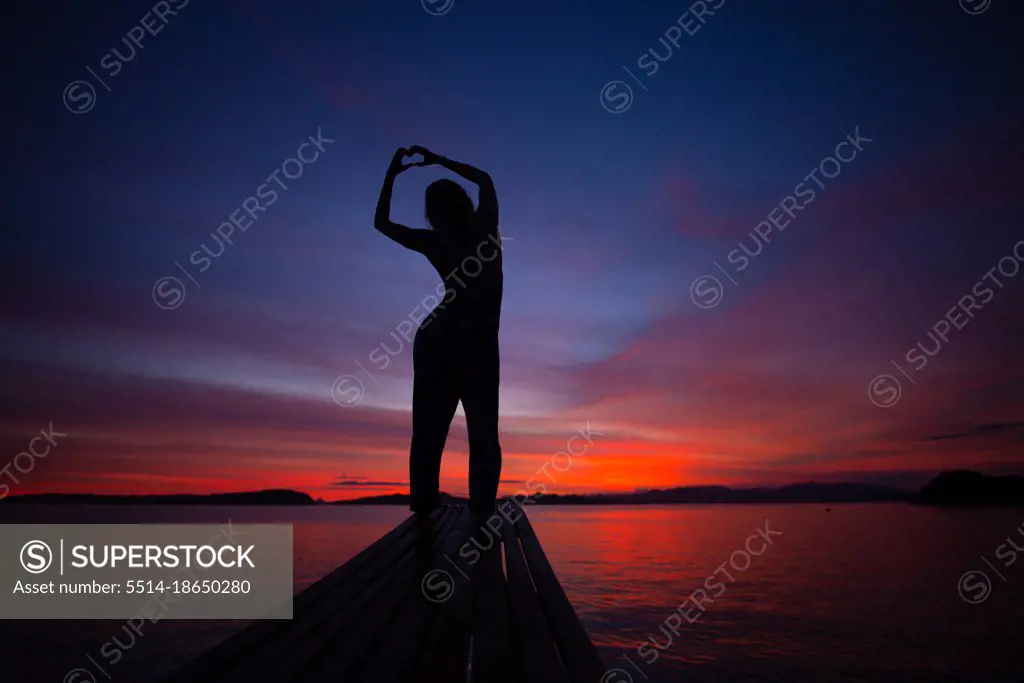 Girl Making A Heart In Front Of Vibrant Sunset In Indonesia