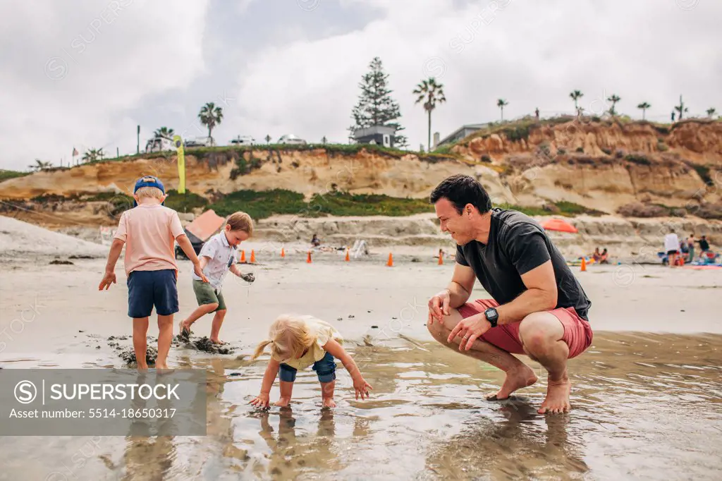 Dad plays happily with kids on Moonlight beach in San Diego