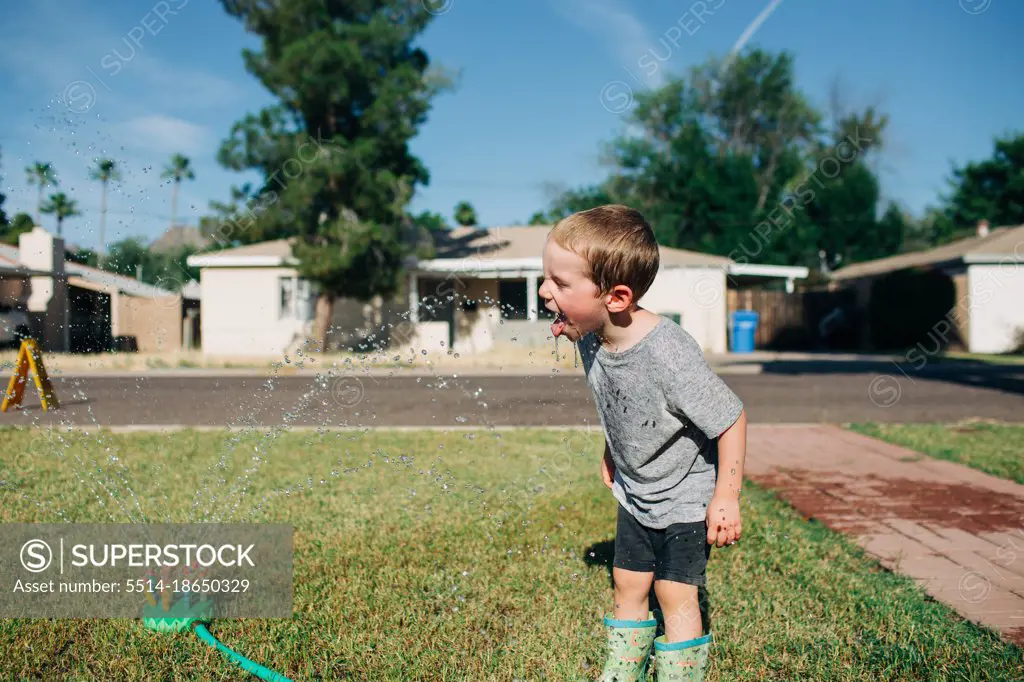 White little boy swallows sprinkler water on hot sunny day