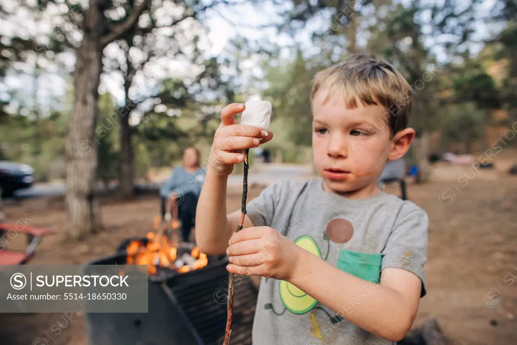 Four year old boy puts marshmallow on stick by campfire