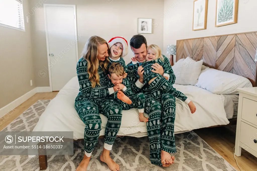 Caucasian family in Christmas pajamas snuggles on bed in Phoenix home