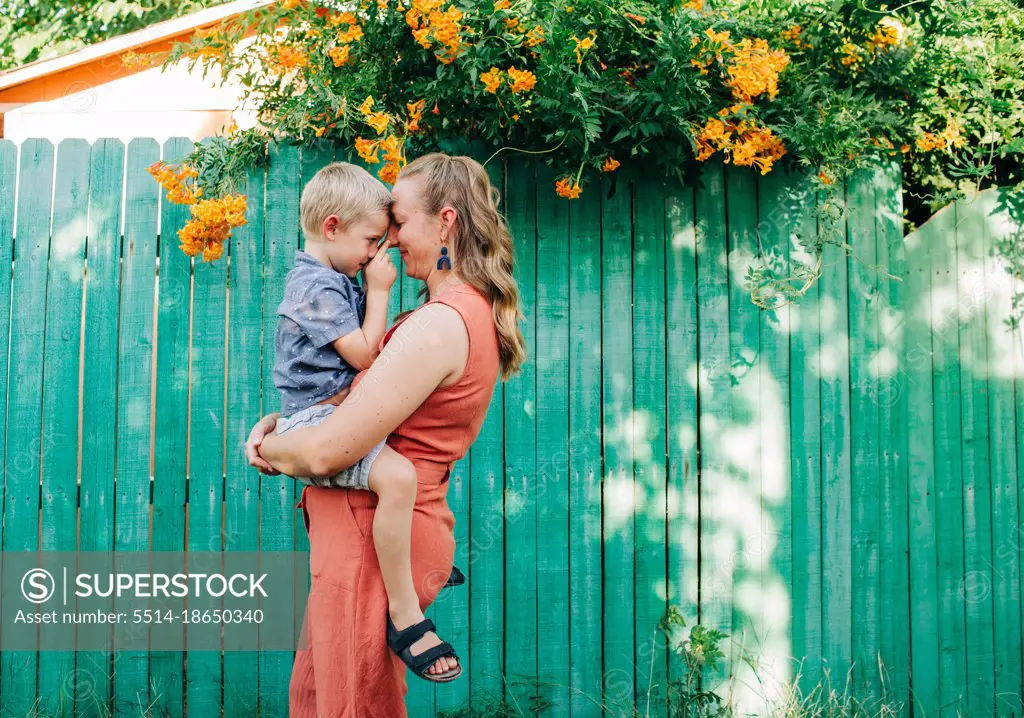 Mother snuggles little boy while standing in front of green fence
