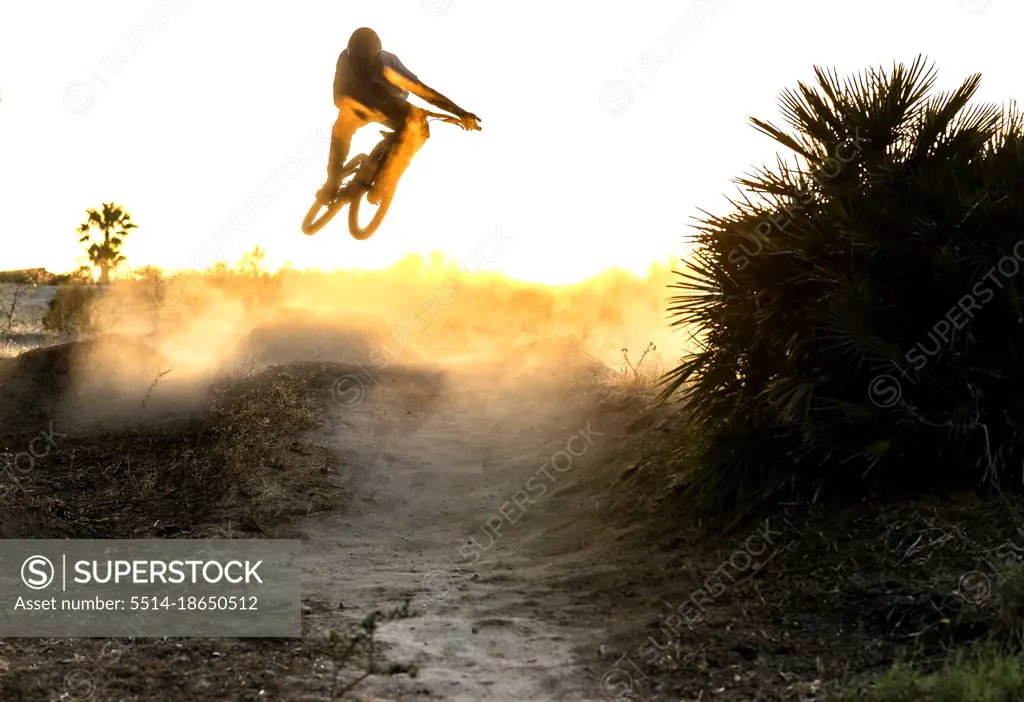 Young mountain biker jumps in a windy and dusty sunset in Spain
