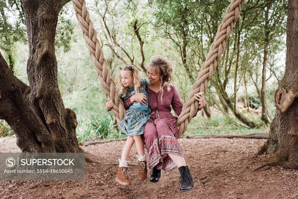 mother and daughter sat on an outdoor swing together hugging