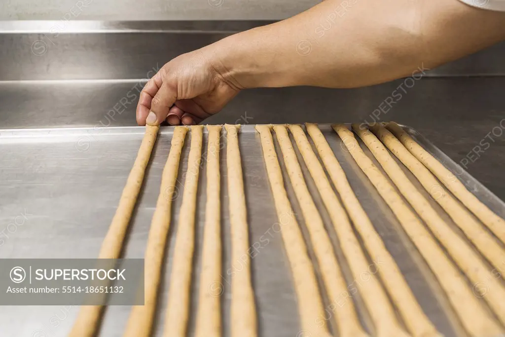 Baker stretching uncooked bread to make strips of artisan bread