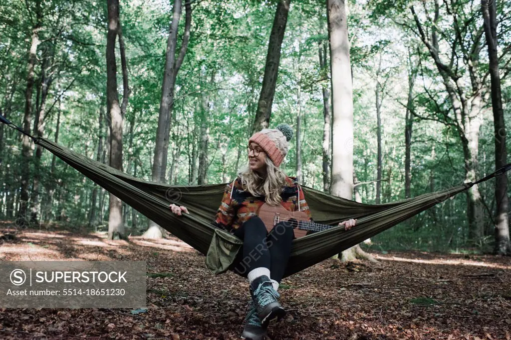 woman sat on a hammock in the forest with a ukulele in autumn