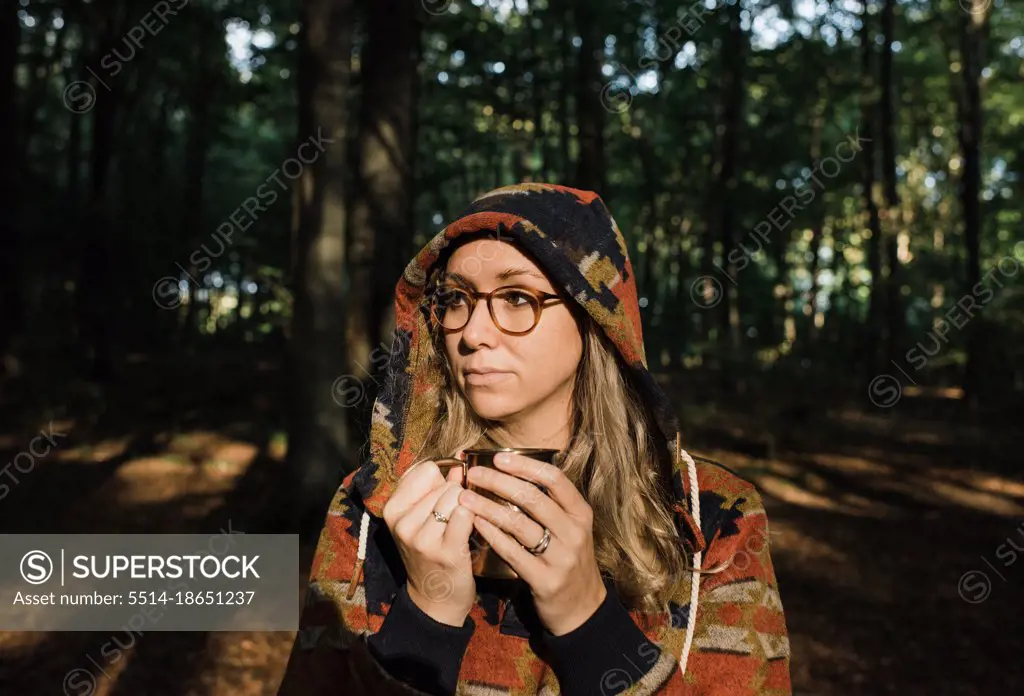 woman stood in forest enjoying hot coffee at sunset