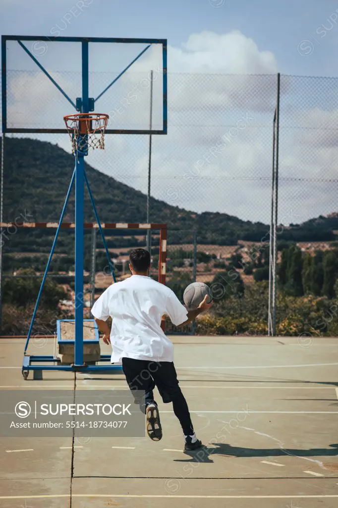 Young boy from his back playing with a basketball on a court