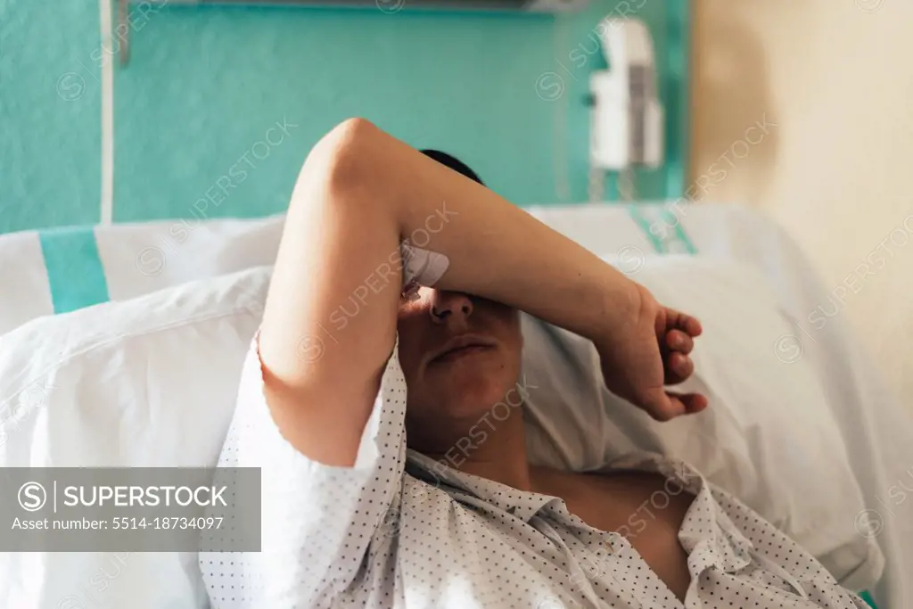 Young woman hospitalized in a bed. Gesture of pain and concern.