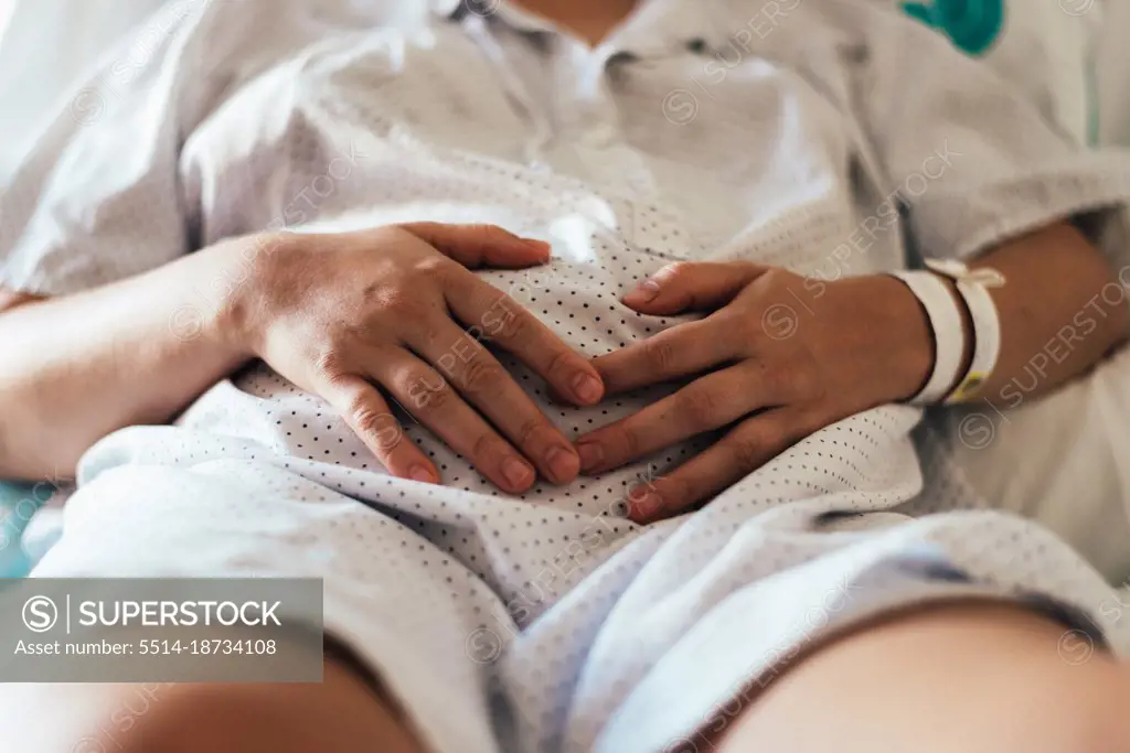 Young woman hospitalized in a bed. Gesture of pain in her belly.