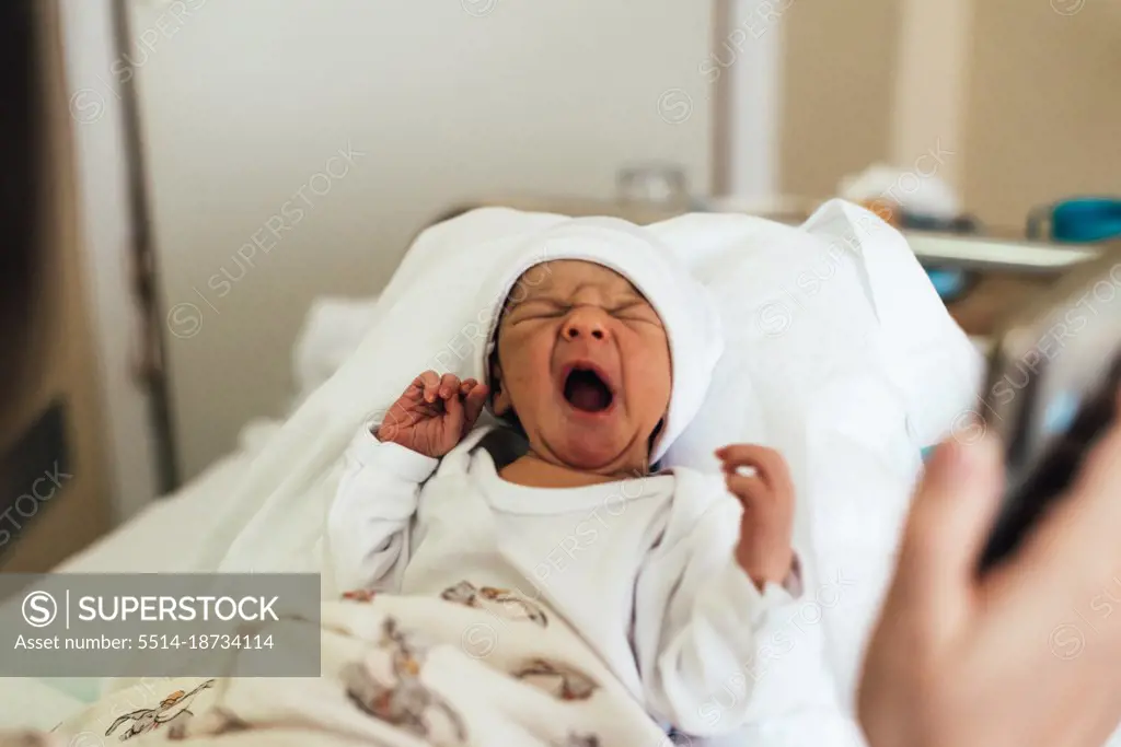 Newborn baby crying in his mother's arms in a hospital bed.