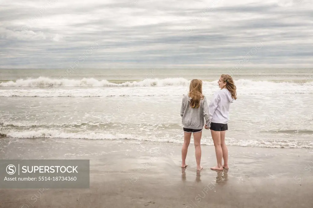 Teen girls in hoodies talk and laugh on windy Florida beach in winter.