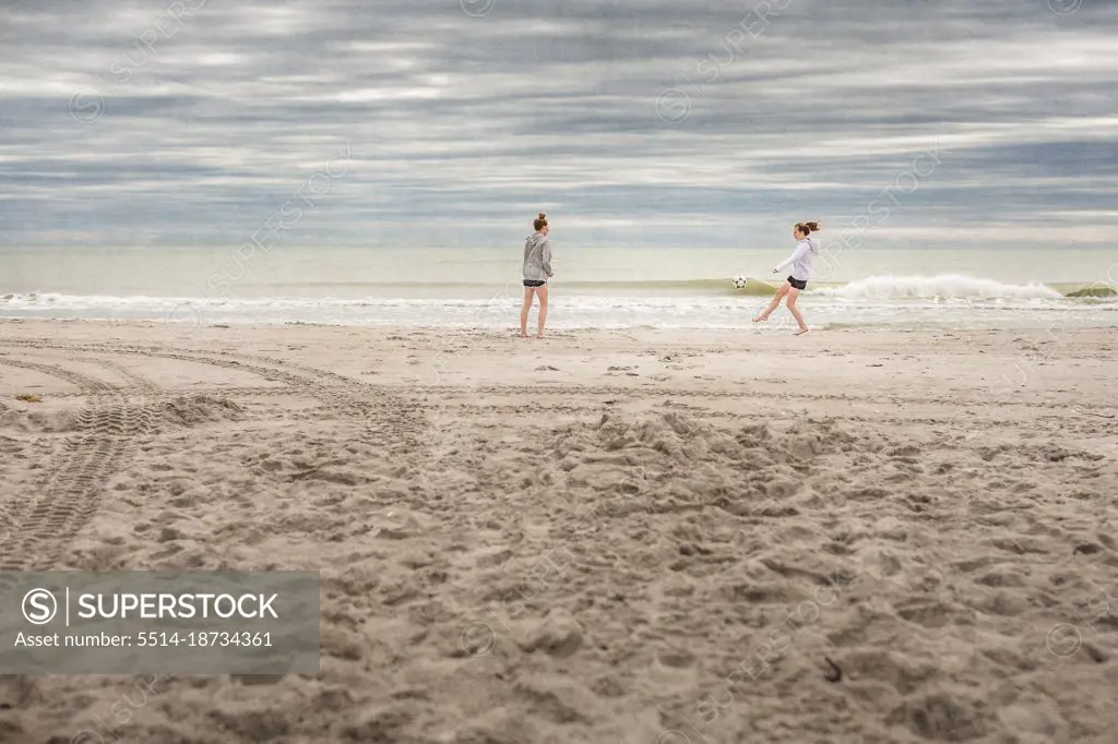 Two girls in hoodies play soccer on a deserted Florida beach in winter