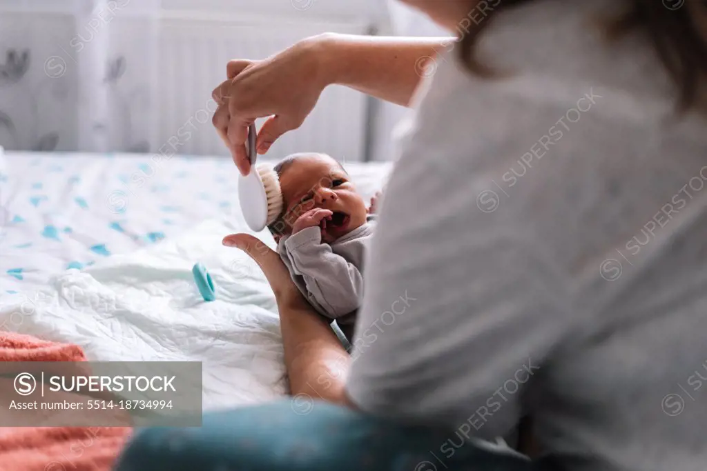 Mother combing her baby's hair in bed.