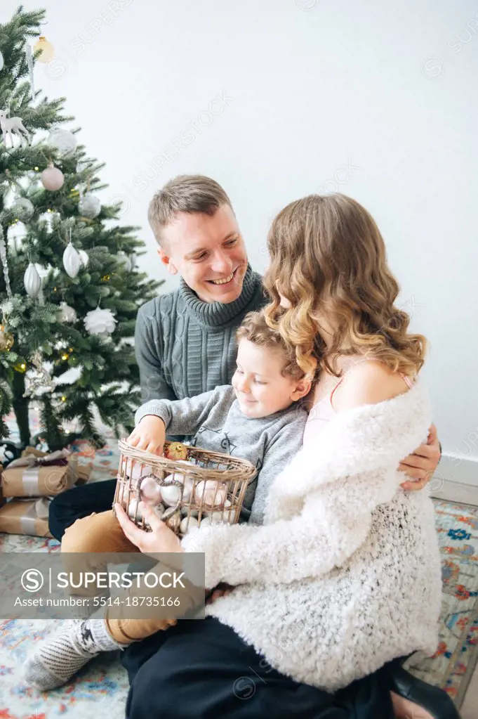 Man hugs his wife, son holds basket with decor for Christmas tree