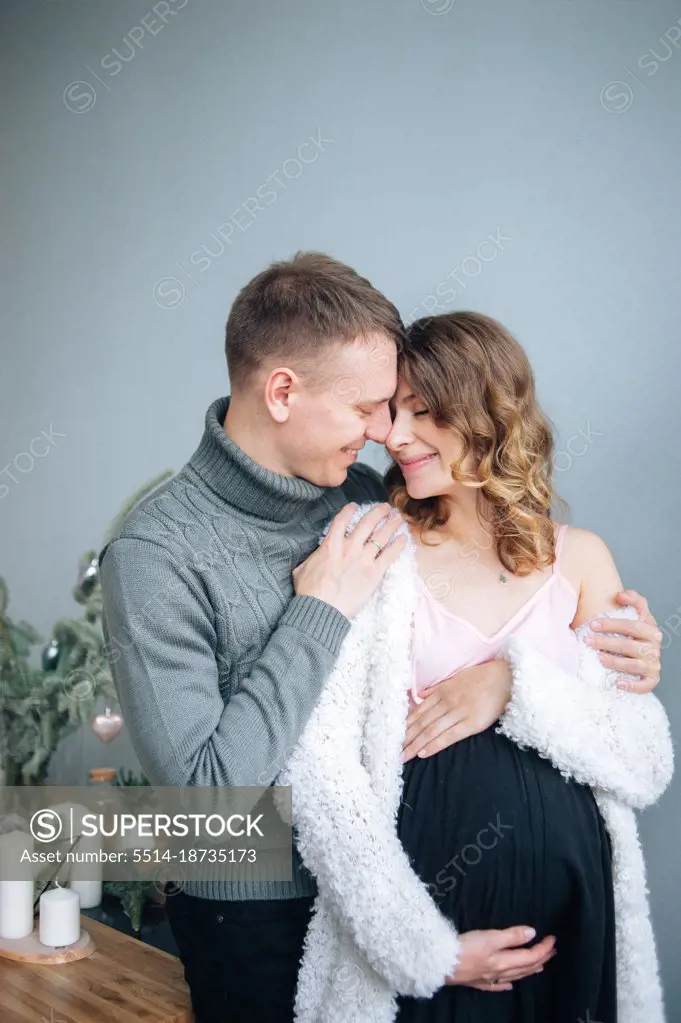 Man hugs his pregnant wife. She hugs her stomack smiling.