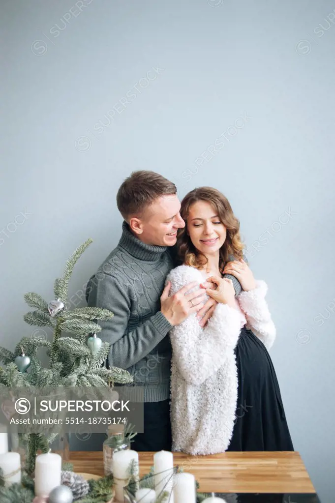 Man hugs his pregnant wife. She hugs his hand on her smiling.