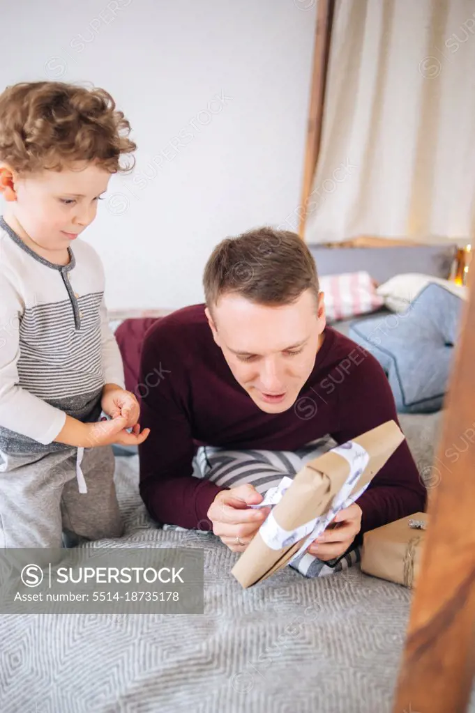 Cute boy and father unwrapping present for Christmas