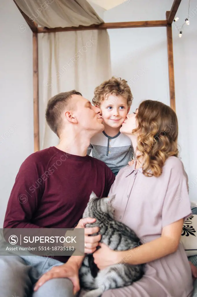 Loving mother and father embrace and kiss baby in cheek