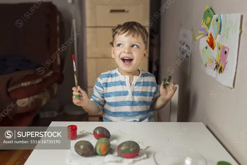 Upper body of blonde boy holding paintbrush and painting easter 