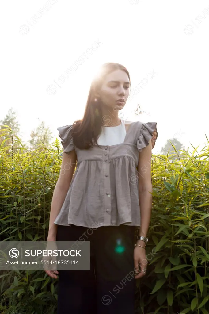 A young girl in a top stands at sunset in the tall grass