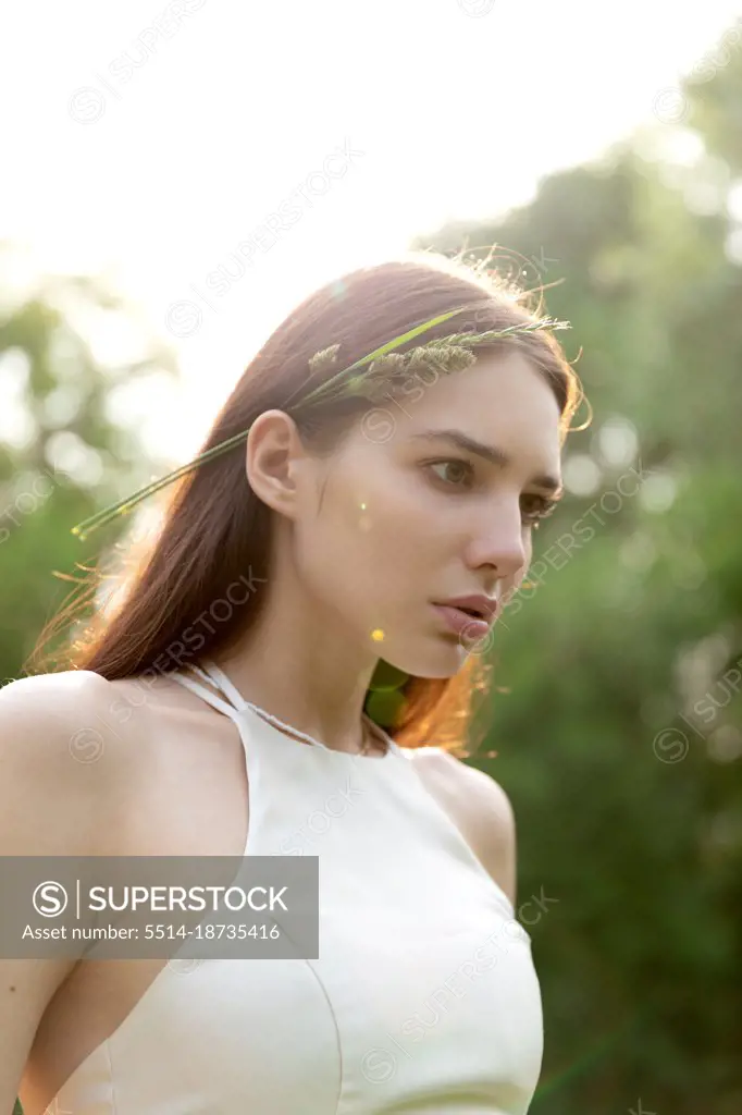 Young woman in the rays of the sunset. blade of grass in her hair
