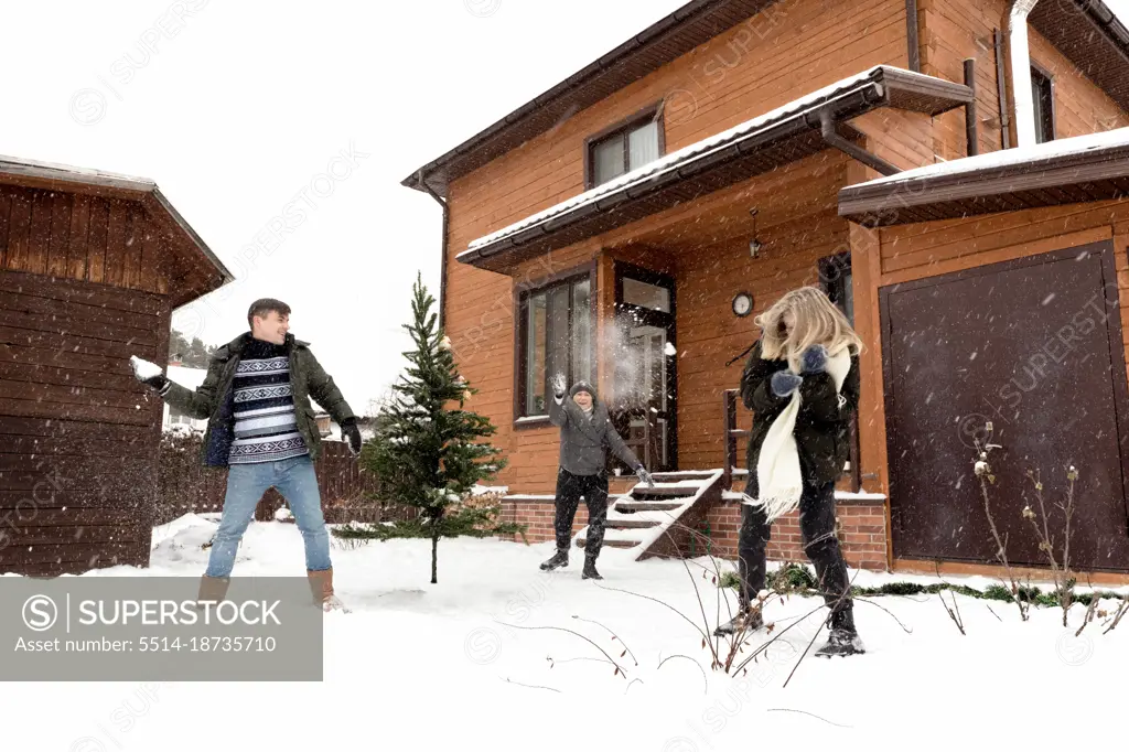 Man, young woman and adult woman playing snowballs near wooden house