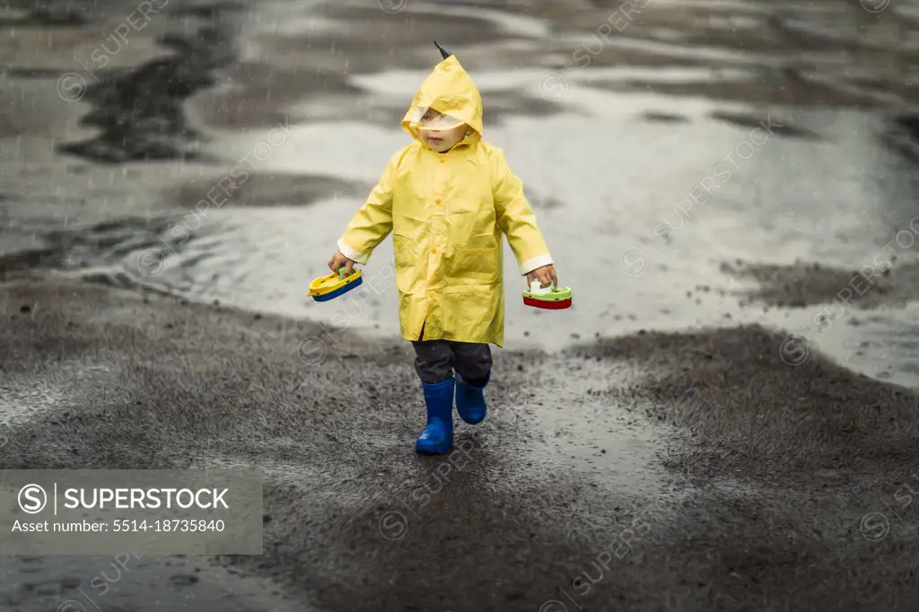 Toddler child in yellow raincoat and blue rain boots walking