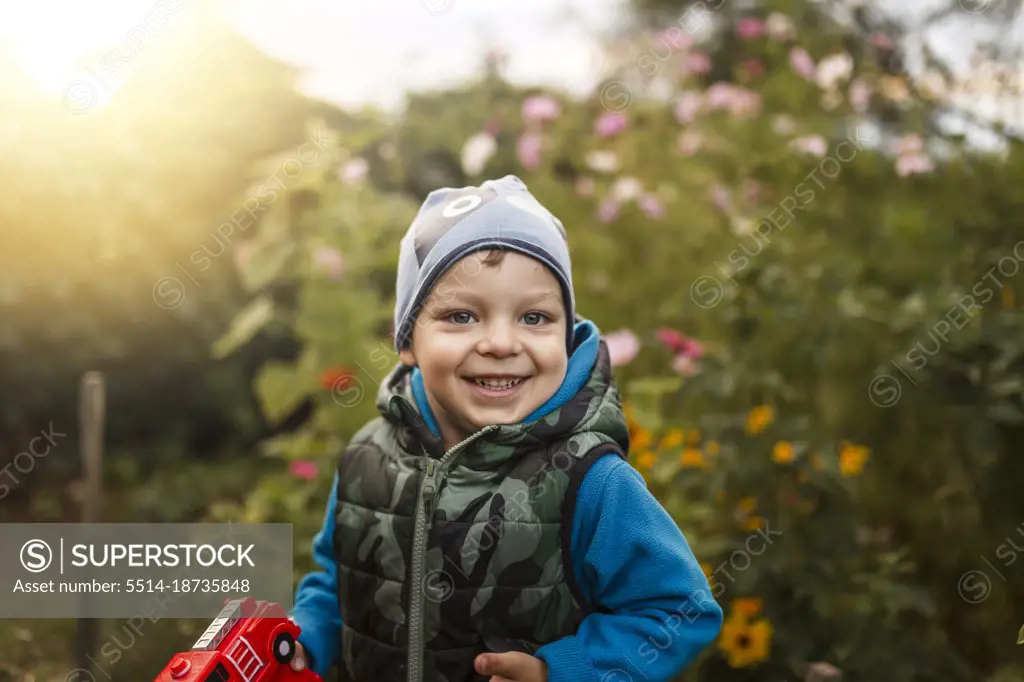 Toddler boy smiling in garden full of flowers wearing blue clothes