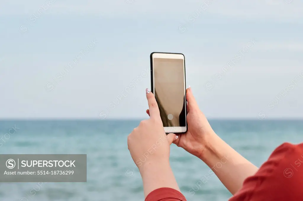 Hands of a person holding a mobile with the sea in the background